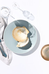 Oyster shell on blue dish. Crystal white tablecloth with glass of water, gray napkin, fork and knife. Minimal seafood cafe table top view. Summer day concept with white table top view.