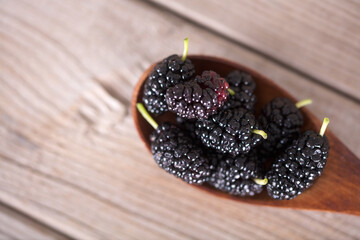 A spoonful of fresh mulberries on a wooden background