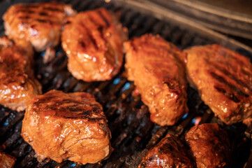 Steaks grilling on a gas barbecue covered in spicy BBQ sauce.