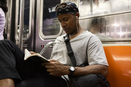 Young adult blackman riding book on the Manhattan subway 