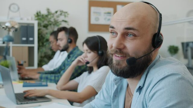 Attractive guy wearing headset is talking to client working in technical customer support in office. Job and professional communication concept.