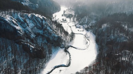 Drone view of the Snow covered street in between the forest in Ojcowski Park Narodowy Krakow, Poland. Daytime time shot during the winter season. Grove of ever green trees on both sides. 