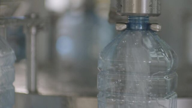 Plastic canister in the water filling machine filled with pure mineral water in the bottling plant