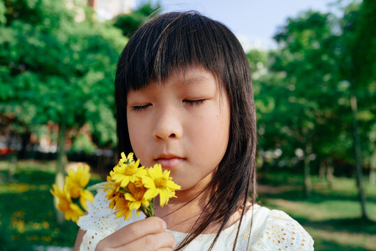 Little girl smelling fresh daisy flowers in the garden
