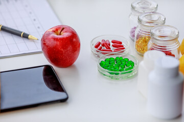 apple, red, green, yellow pills in several bottles, mobile phone and pen on nutritionist table with weekly eating plan. Concept for nutritions table top view photography.