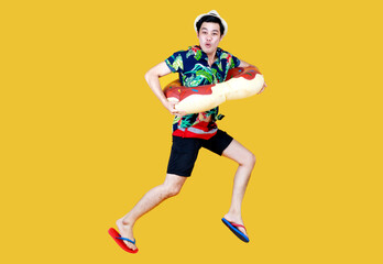 Fototapeta na wymiar Young attractive Asian man wearing green and blue Hawaiian shirt and donut swim ring around his waist running against yellow background. Concept for holiday beach vacation