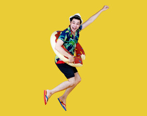 Fototapeta na wymiar Young attractive Asian man wearing green and blue Hawaiian shirt and donut swim ring around his waist running against yellow background. Concept for holiday beach vacation