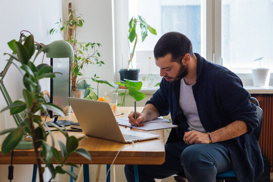Unrecognizable young adult man writing in notebook 