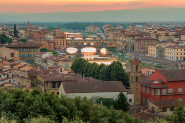 Fototapeta na wymiar Florence, Italy - 20 June, 2019 : panoramic overview from Arnolfo Tower (Torre di Arnolfo)at sunset haze, historical part of the city, River Arno and mountains range in sunset rays on the background 