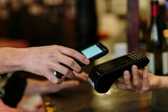 Detail shot of hand holding a smart phone doing a wireless payment at a restaurant