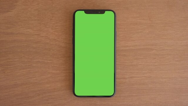 Smartphone place on wood table, Green screen telephone, Close up display mobile phone with mock up, Chroma key monitor, Close-up the cell phone on brown desktop, Mockup smartphone, Zoom top view.