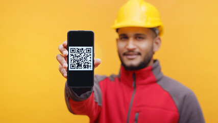 Delivery man wearing yellow helmet and uniform showing mobile phone to the camera with QR code on...