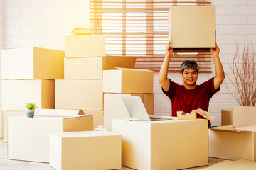 Fototapeta premium Portrait asian guy men sit in the house and there are a lot of boxes in the house : Playful handsome man with an empty box on top of his head is happy with his new home.