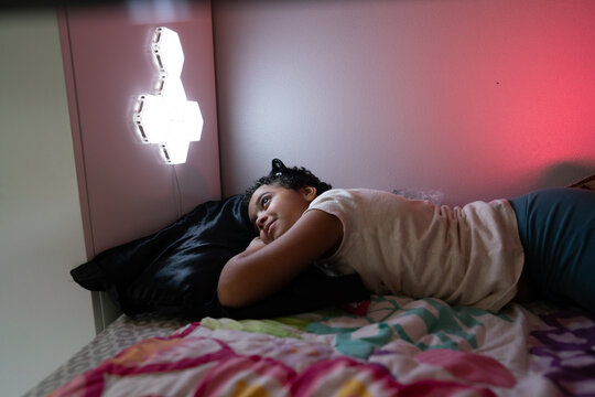 Mixed race girl lays on bed staring at wall lamp