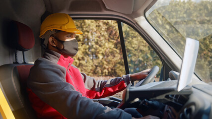 Man wearing yellow helmet and a mask driving a van. Focused man with hands on steering wheel...
