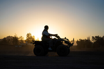 Silhouette of a tourist woman rides a quad bike against background of a bright sunset. Evening...