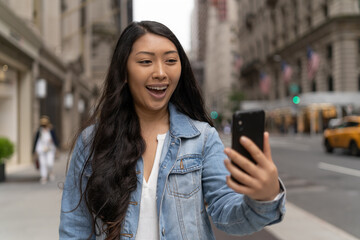 Young Asian woman in city walking face time video chatting