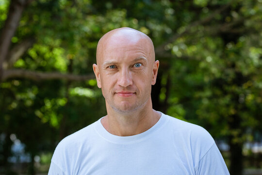 portrait of a bald man in a white T-shirt on the background of the park, mimicry raised eyebrow