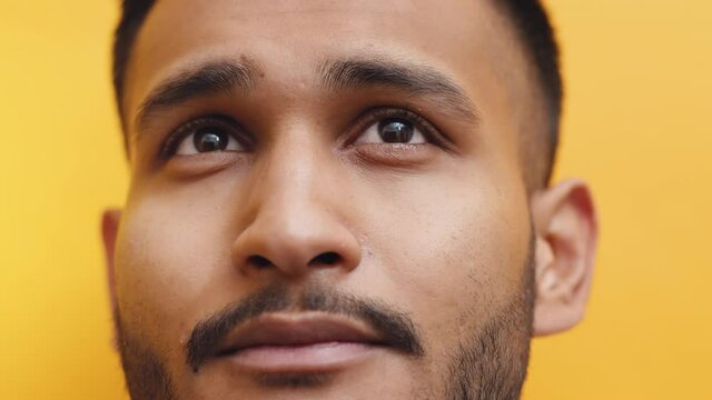 Young Indian guy looking at something thoughtfully. Closeup footage of a guy with beard shot in the studio with yellow background. High quality.
