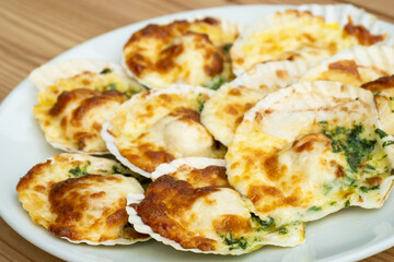 Baked parmesan scallops in a white ceramic plate on a wooden table . Oven baked scallop with...