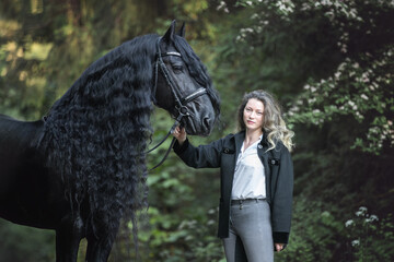 Happy young woman with the frisian horse in the summer forest. - 439769062
