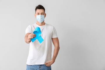 Man with blue ribbon on light background. Prostate cancer awareness concept