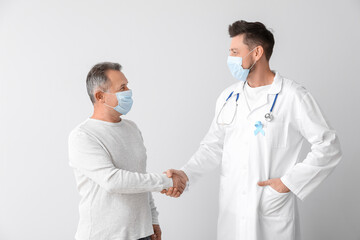 Doctor and mature man shaking hands on light background. Prostate cancer awareness concept