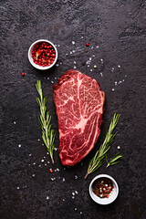 Fresh marbled beef rib eye steak and spices on black stone background