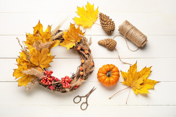 Beautiful autumn wreath with craft supplies on white wooden background