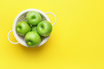 Colander with fresh green apples on color background