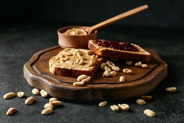 Board with tasty peanut butter and bread on dark background