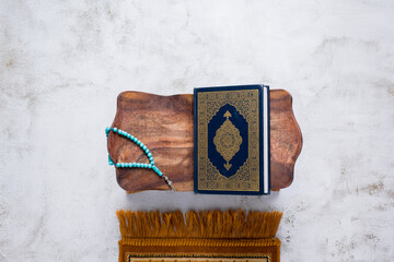 Islamic concept - The Holy Al Quran with written Arabic calligraphy meaning of Al Quran and rosary beads or tasbih and prayer rug, on wooden stand, with copy space.
