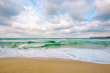 cloudy seascape scenery in evening light. waves crush on the sandy beach. dramatic weather nature background