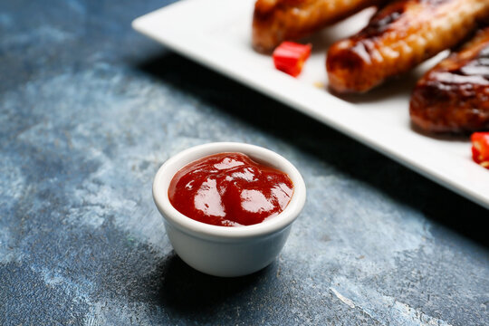 Roasted chicken wings and barbecue sauce on color background