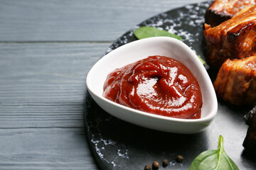 Bowl with tasty barbecue sauce and roasted pork on dark wooden background