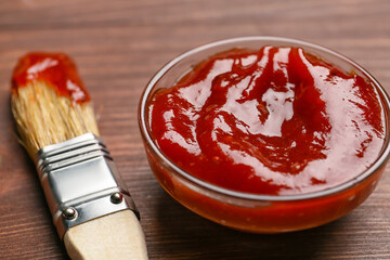 Bowl with tasty barbecue sauce and brush on wooden background