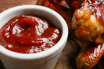 Roasted chicken wings and barbecue sauce on wooden background, closeup
