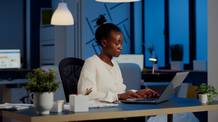 Busy african manager working on financial reports checking statistics graphs, typing on laptop...