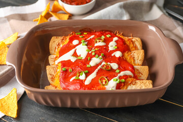 Baking dish with tasty cooked enchilada on table