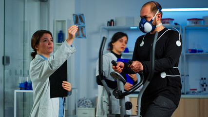 Team of doctor researchers monitoring endurance of man performance sports wearing mask running cross trainer. Lab science doctor measuring vo2 of sportsman, looking at x-ray explaning health status