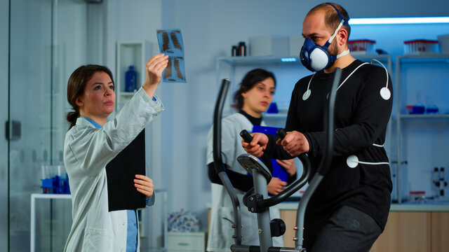 Team of doctor researchers monitoring endurance of man performance sports wearing mask running cross trainer. Lab science doctor measuring vo2 of sportsman, looking at x-ray explaning health status