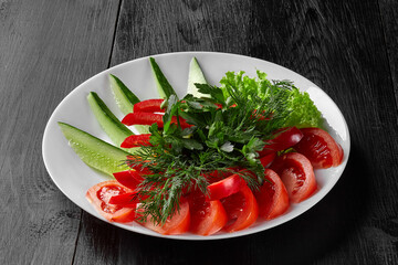 Sliced tomato, sweet pepper, cucumber and greens on plate