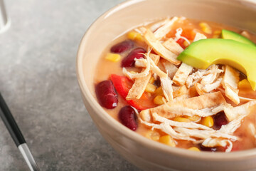 Bowl of tasty chicken enchilada soup on table, closeup
