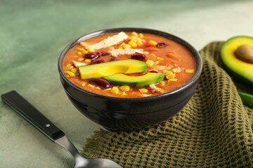 Bowl of tasty chicken enchilada soup on color background