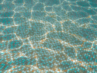 Tiles at the bottom of the pool. Transparent water distorts the multicolored geometric pattern. Sun glare on the ripples of the water surface