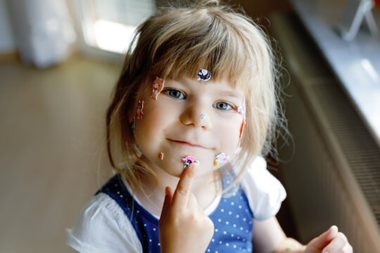 Little toddler girl playing with different colorful animal stickers. Concept of activity of children during pandemic corona virus quarantine. Happy funny child having fun with stick stickers on face.