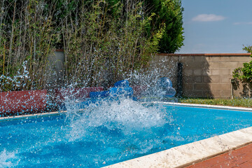 A huge splash of water is created by the cannonball dive into a swimming pool