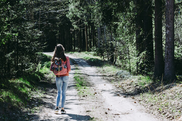 One young girl tourist with backpack walking on path through forest during summer day. Hipster lifestyle and solo trip.