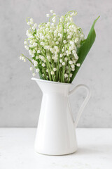 Jug with beautiful lily-of-the-valley flowers on light background