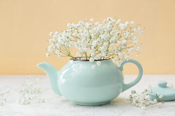 Teapot with beautiful gypsophila flowers on table near color wall, closeup
